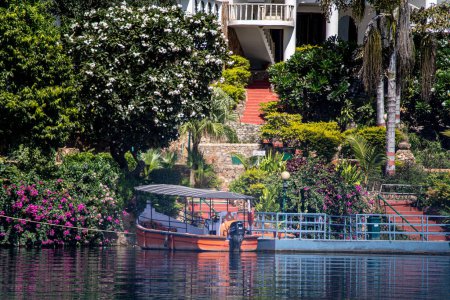 Photo for Boat tied standing in the middle of beautiful flower and tree shaded cove with blue railings showing the beautiful Dehbar lake in jaisamand udaipur India - Royalty Free Image