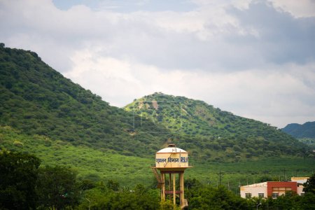 Aravalli range in jaipur rajasthan with small hills mountains covered in green trees under monsoon clouds with water tank and buildings India