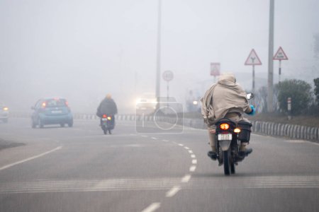 Foto de Delhi, India - circa 2023: men on motorcycle covered with shawls riding on cold winter morning in dense fog with limited traffic in delhi, haryana, rajasthan India - Imagen libre de derechos