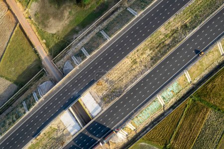 Photo for Aerial drone shot moving along and shooting straight down of new delhi mumbai jaipur express elevated highway showing six lane road with green feilds with rectangular farms on the sides - Royalty Free Image
