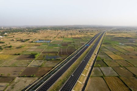 Photo for Locked tripod aerial drone shot of new delhi mumbai jaipur express elevated highway showing six lane road with green feilds with rectangular farms on the sides - Royalty Free Image