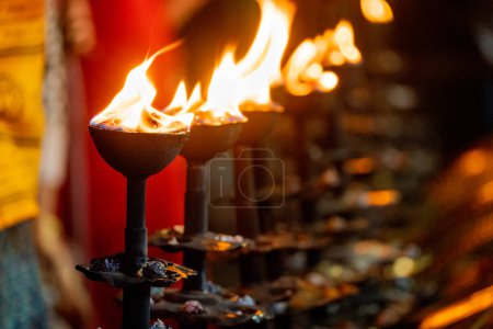 LIne of fire oil lamps on the ghat of ganga in rishikesch, wo Menschen den Segen empfangen, indem sie ihre Hände über das Feuer im Hinduismus reichen
