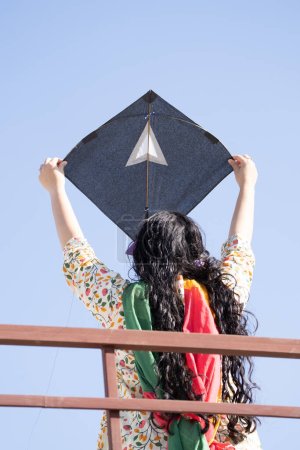 Téléchargez les photos : Jeune fille en vêtements indiens traditionnels tenant cerf-volant noir haut au-dessus de la tête le lançant sur les célébrations de la fête de l'indépendance de la république de Sankranti - en image libre de droit