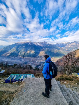 Photo for Male trekker hiker standing looking down at village houses and himalaya mountains in distance and cloudy sky in manali, kullu, shimla, kedarnath in India - Royalty Free Image