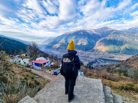 Wanderin, die auf Dorfhäuser und Himalaya-Berge in der Ferne und wolkenverhangenen Himmel in Manali, Kullu, Shimla, Kedarnath in Indien blickt