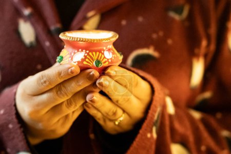 Mujer joven sosteniendo diya decorado que parece una olla de barro en la víspera de diwali dussera una manera de traer luz sobre el festival en la India