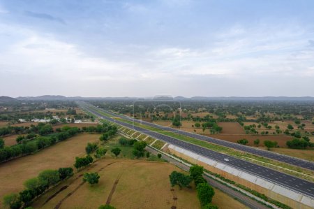 dron aéreo elevándose sobre estanques y campos verdes con autopista delhi mumbai que se extiende hacia la distancia con nubes teñidas de rosa al atardecer que muestran el hermoso paisaje de la India y viajan