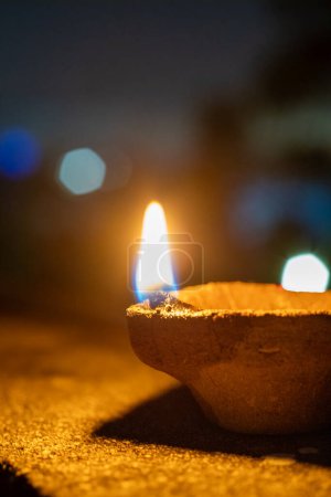 handmade earthenware clay coconut fiber diya lamp lit in front of the soft focussed bokeh lights of diwali major celebration in India