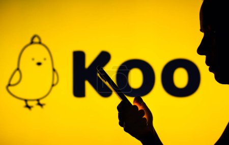 Foto de 18 de noviembre de 2022, Brasil. En esta ilustración de la foto, el logotipo de la aplicación Koo se ve en el fondo de una mujer silueta sosteniendo un teléfono móvil - Imagen libre de derechos