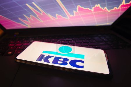 Photo for March 21, 2023, Brazil. In this photo illustration the KBC Bank logo seen displayed on a smartphone screen, with graphic representation of the stock market in the background - Royalty Free Image