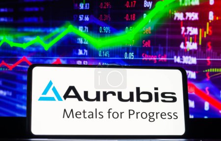 Foto de 22 de marzo de 2023, Brasil. En esta ilustración fotográfica, el logotipo de Aurubis AG se muestra en una pantalla de teléfono inteligente, con representación gráfica del mercado de valores en el fondo. - Imagen libre de derechos