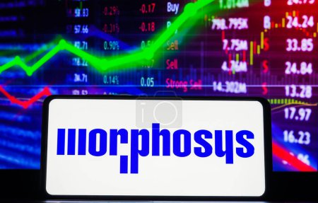 Foto de 22 de marzo de 2023, Brasil. En esta ilustración fotográfica, el logotipo de MorphoSys AG se muestra en una pantalla de teléfono inteligente, con representación gráfica del mercado de valores en el fondo. - Imagen libre de derechos