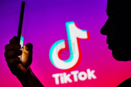 Foto de 6 de abril de 2023, Brasil. En esta ilustración fotográfica, la silueta de una mujer sostiene un teléfono inteligente con el logotipo de TikTok en el fondo - Imagen libre de derechos