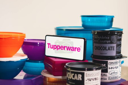 Foto de 12 de abril de 2023, Brasil. En esta ilustración fotográfica, una pila de varios productos de plástico junto a un teléfono inteligente que muestra el logotipo de Tupperware - Imagen libre de derechos