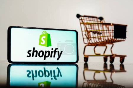 Foto de 8 de mayo de 2023, Brasil. En esta ilustración fotográfica, el logotipo de Shopify se muestra en un teléfono inteligente junto con un carrito de compras - Imagen libre de derechos