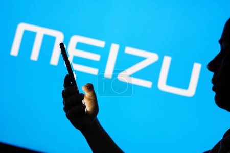 Photo for June 13, 2023, Brazil. In this photo illustration, the Meizu logo is seen in the background of a silhouetted woman holding a mobile phone - Royalty Free Image