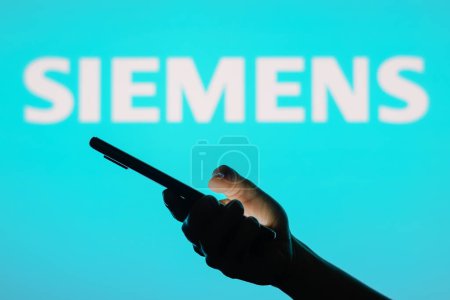 Téléchargez les photos : 13 juin 2023, Brésil. Sur cette photo, le logo Siemens vu à l'arrière-plan d'une femme silhouette tenant un téléphone portable - en image libre de droit