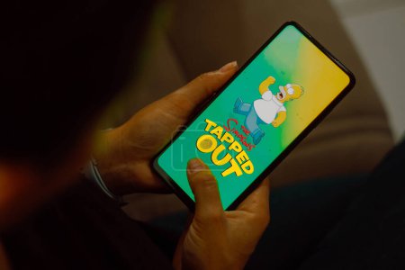 Foto de 10 de julio de 2023, Brasil. En esta ilustración fotográfica, el logotipo Simpsons: Tapped Out se muestra en la pantalla de un teléfono inteligente - Imagen libre de derechos