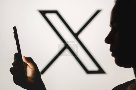 Foto de 24 de julio de 2023, Brasil. En esta ilustración fotográfica, la silueta de una mujer sostiene un teléfono inteligente con el nuevo logotipo de Twitter (X) en el fondo - Imagen libre de derechos