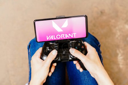 Photo for August 8, 2023, Brazil. In this photo illustration, a person playing on a joystick and the Valorant logo displayed on a smartphone screen - Royalty Free Image