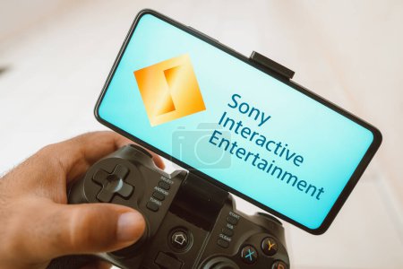 Photo for August 11, 2023, Brazil. In this photo illustration, a person plays on a joystick and the Sony Interactive Entertainment logo displayed on a smartphone screen - Royalty Free Image