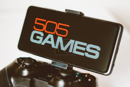Photo for August 14, 2023, Brazil. In this photo illustration, the 505 Games logo displayed on a smartphone screen, connected to a gaming joystick - Royalty Free Image