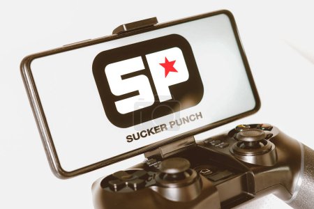 Photo for August 14, 2023, Brazil. In this photo illustration, the Sucker Punch Productions logo displayed on a smartphone screen, connected to a gaming joystick - Royalty Free Image
