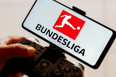 Foto de 15 de agosto de 2023, Brasil. En esta ilustración fotográfica, una persona juega en un joystick de juego y el logotipo de la Bundesliga se muestra en la pantalla de un teléfono inteligente - Imagen libre de derechos