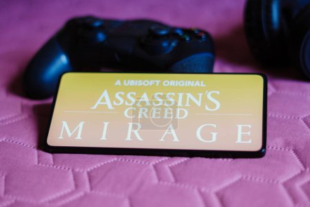 Téléchargez les photos : 9 octobre 2023, Brésil. Dans cette illustration photo, le logo Assassin's Creed Mirage est affiché sur un écran de smartphone, à côté d'une manette de jeu. - en image libre de droit