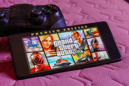 Photo for October 9, 2023, Brazil. In this photo illustration, the Grand Theft Auto V (GTA) logo is displayed on a smartphone screen, next to a gamepad - Royalty Free Image