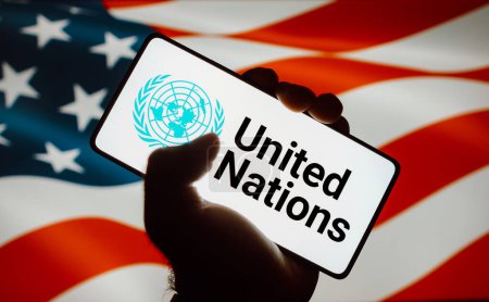 Foto de 12 de octubre de 2023, Brasil. En esta ilustración fotográfica, el logotipo de las Naciones Unidas (ONU) se muestra en una pantalla de teléfono inteligente y en el fondo la bandera de los Estados Unidos (EE.UU.) - Imagen libre de derechos