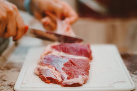 Foto de La grasa de la carne roja es quitada por el cocinero. La carne roja tiene una gran cantidad de vitaminas del complejo B, E, K y zinc, hierro, proteínas - Imagen libre de derechos