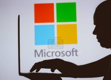 Photo for January 9, 2024, Brazil. In this photo illustration, the Microsoft logo is seen in the background of a silhouette of a person using a notebook - Royalty Free Image