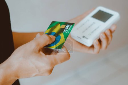 Téléchargez les photos : 17 janvier 2024, Brésil. Sur cette photo, une femme tenant la carte Auxlio Brasil (Bolsa Famlia) et la machine à cartes de crédit. - en image libre de droit