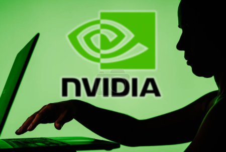 Photo for March 28, 2024, Brazil. In this photo illustration, the Nvidia logo is seen in the background of a silhouette of a person using a notebook - Royalty Free Image
