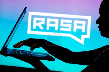 Foto de 29 de marzo de 2024, Brasil. En esta ilustración fotográfica, el logotipo de Rasa Technologies se ve en el fondo de una silueta de una persona usando un cuaderno - Imagen libre de derechos