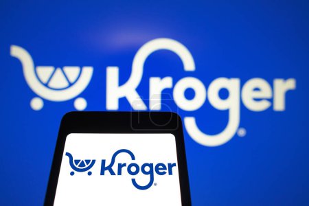 Foto de 31 de marzo de 2024, Brasil. En esta ilustración fotográfica, el logotipo de Kroger se muestra en la pantalla de un teléfono inteligente y en el fondo - Imagen libre de derechos