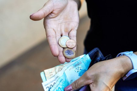 Foto de 19 de abril de 2024, Brasil. La mujer guarda monedas de verdad en su billetera. Según datos oficiales, el ingreso promedio de los hogares per cápita (por persona) aumentó a R $1,848 por mes en Brasil - Imagen libre de derechos