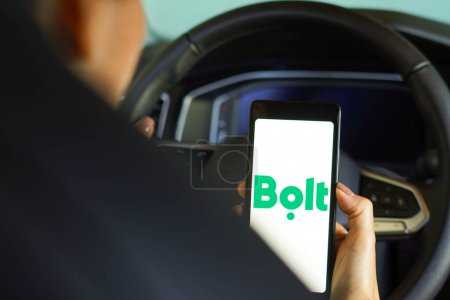 Photo for April 20, 2024, Brazil. In this photo illustration, the driver holds the steering wheel and a smartphone displaying the Bolt logo. It is a technology company providing mobility services, car rental, car sharing and food delivery services based in Tal - Royalty Free Image