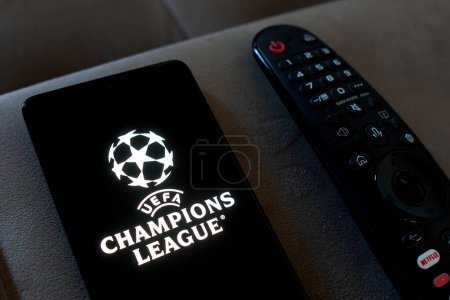 Téléchargez les photos : May 6, 2024, Brazil. In this photo illustration, the logo of the UEFA Champions League seen displayed on a smartphone next a TV remote control. - en image libre de droit