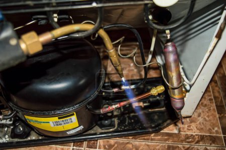 Sauerstoffgasschweißen während der Reparatur eines Kühlschranks. Sauerstoffschweißen. Kühlaggregatmotor. Wartungsarbeiten. Reparaturwerkstatt für Haushaltsgeräte. Industrielle Geräte.