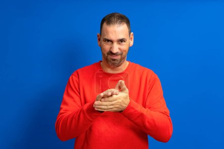 Foto de Latino handsome man feeling proud, mischievous and arrogant while hatching an evil plan or thinking up a trick. Isolated on blue background - Imagen libre de derechos