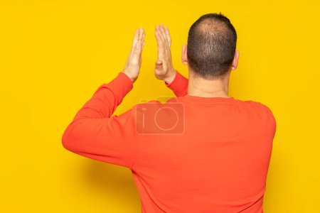 Photo for Half-bald man energetically clapping his back, he is excited about the spectacle he has just witnessed. Isolated on yellow background - Royalty Free Image