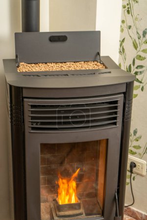 Vertical image of a modern pellet stove with the hopper full to overflowing, ecological and sustainable heat, renewable energy.