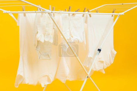 Drying rack with different clothes on yellow background