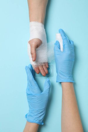 Foto de Concepto de ayuda durante una lesión, médico envolviendo la mano en un vendaje sobre fondo azul - Imagen libre de derechos