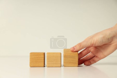 Photo for Three wooden cubes on white table and female hand, close up - Royalty Free Image