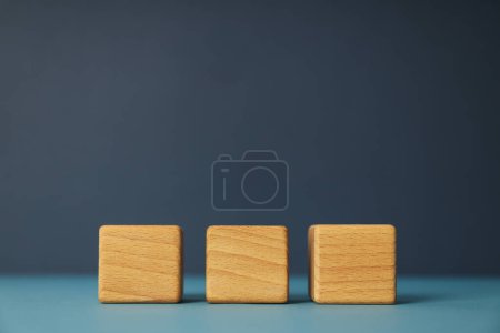 Photo for Three wooden cubes on blue table, space for text - Royalty Free Image