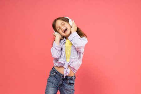 Photo for A little girl in headphones on a pink background listens to music - Royalty Free Image
