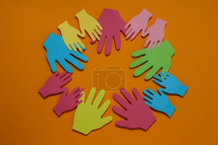 Téléchargez les photos : Les mains sont découpées dans du papier multicolore sur un fond orange - en image libre de droit
